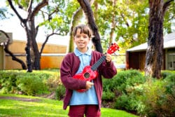 Student playing a bright red ukulele in the school garden