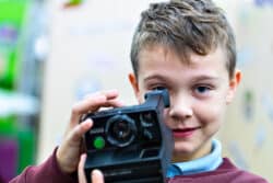 Student facing forward, looking through a Polaroid camera lens