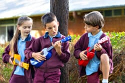 Three students hold ukulele in the outside in the school grounds
